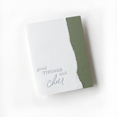 White and green card with a curved torn edge where the two colors meet. Green text saying, “Good Tidings and Cheer”. A white envelope is included.