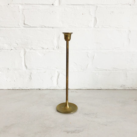 Large brass candlestick with round base and skinny stem; upside down bell shaped top.