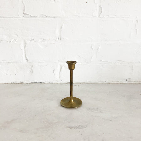 Medium brass candlestick with round base and skinny stem; upside down bell shaped top.