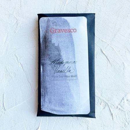 Packaged in a black rectangle pouch with white and gray label with black and red text saying, “Gravesco Madagascar Vanilla Wax Melt”.