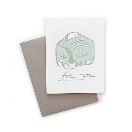 White card with gray text saying, “A Toast for You”. Image of a teal toaster with a slice of bread popping out. A gray envelope is included.