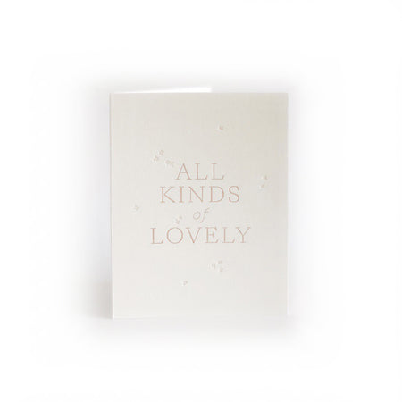 Ivory card with pink text saying, “All Kinds of Lovely”. Images of small embossed flowers scattered across card. An envelope is included.