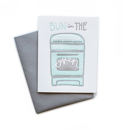 White card with teal and gray text saying, “Bun in the Oven”. Image of a vintage teal colored stove and oven. A gray envelope is included.
