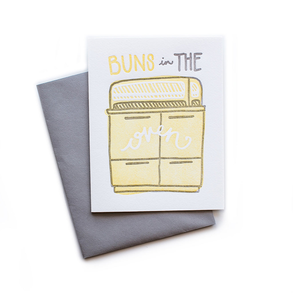 White card with yellow and gray text saying, “Buns in the Oven”. Image of a vintage yellow stove and oven. A gray envelope in included.