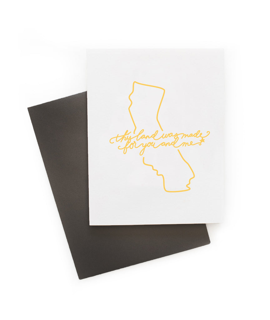 White card with yellow text saying, “This Land is Made for You and Me”. Yellow outline image of the state of California. A gray envelope is included.