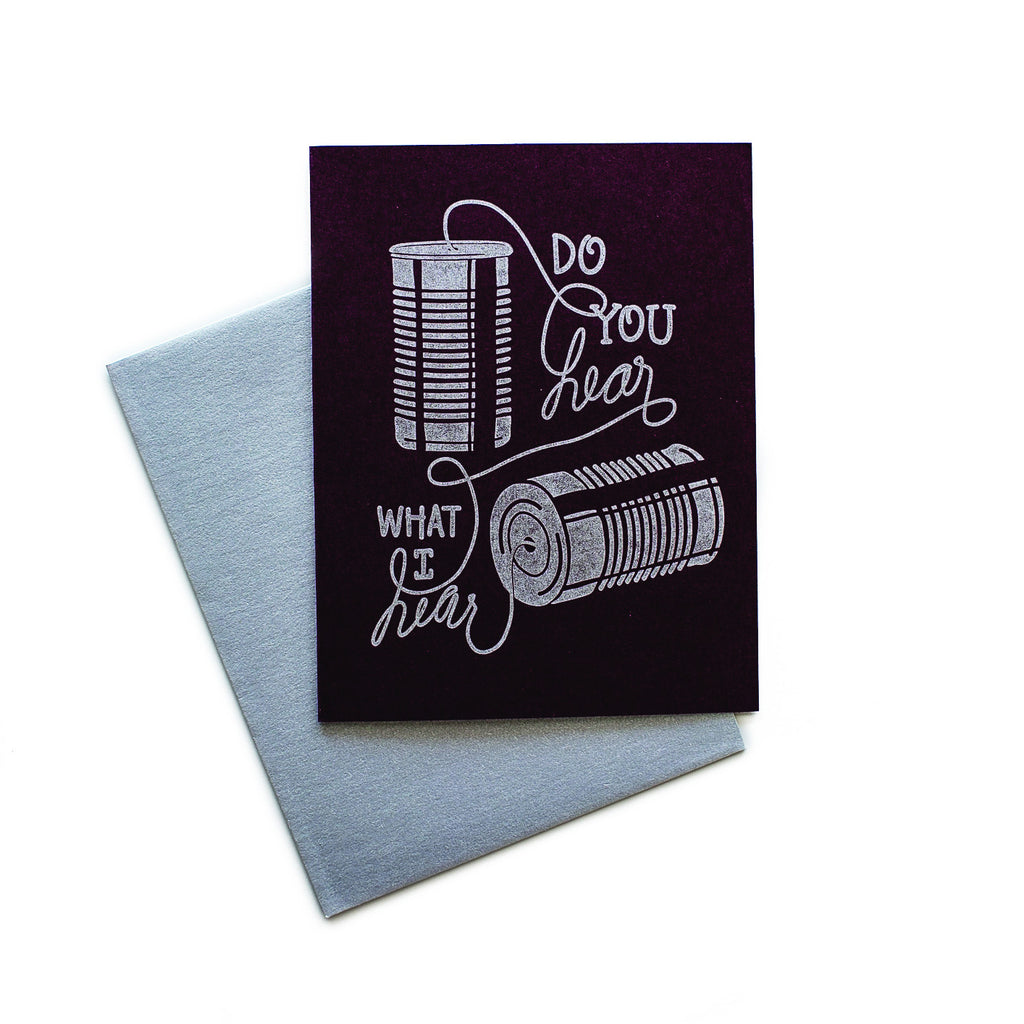 Black card with silver text saying, “Do You Hear What I Hear”. Images of vintage tin can with string telephone system. A silver envelope is included.