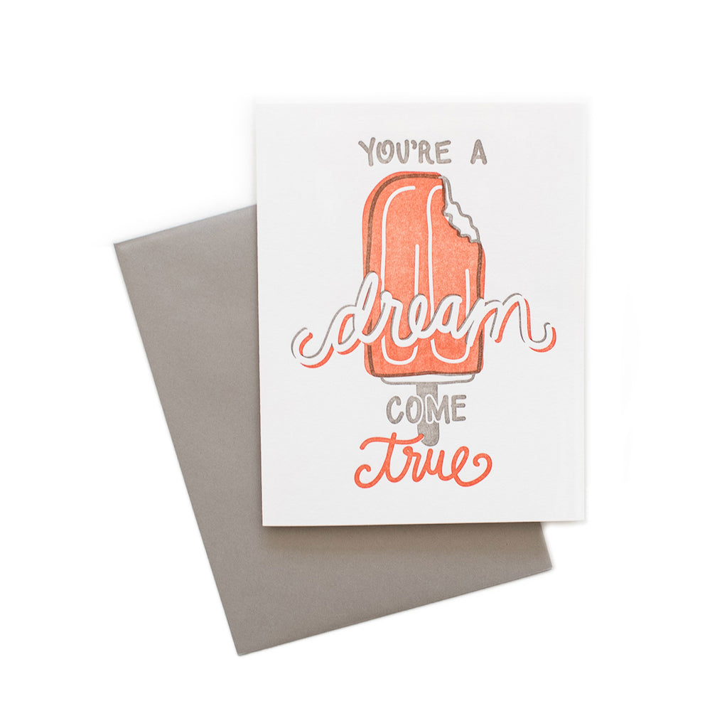 White card with gray and orange text saying, “You’re A Dream Come True”. Image of an orange creamsicle ice cream with a bite taken out of right side. A gray envelope is included.