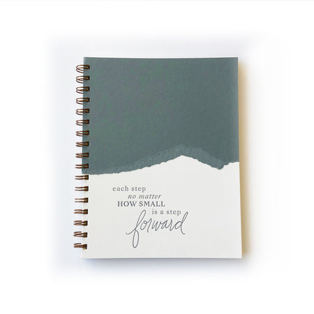 Ivory and green cover with a curved line where two colors meet. Green text saying, “Each Step No Matter How Small Is A Step Forward”. Gold spiral on left side of notebook.