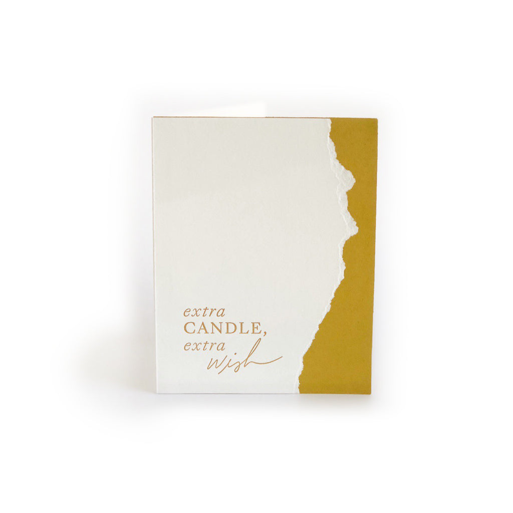 Ivory card with gold stripe down right side. Gold text saying, “Extra Candle, Extra Wish”. An ivory envelope is included.