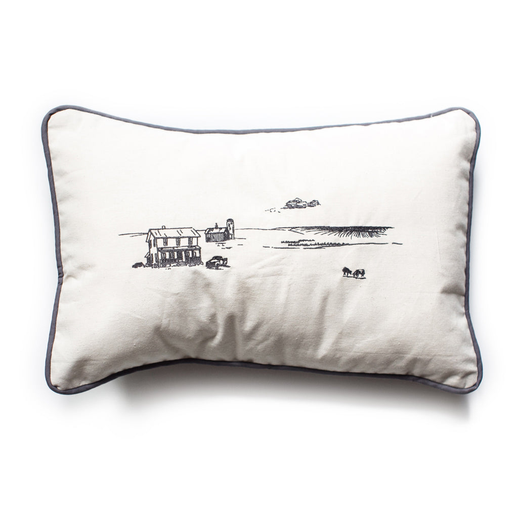 Ivory pillow with black ink. Image of a farm including: farmhouse, barn with silo; windmill; crops in field; and cows in field. Black edging.