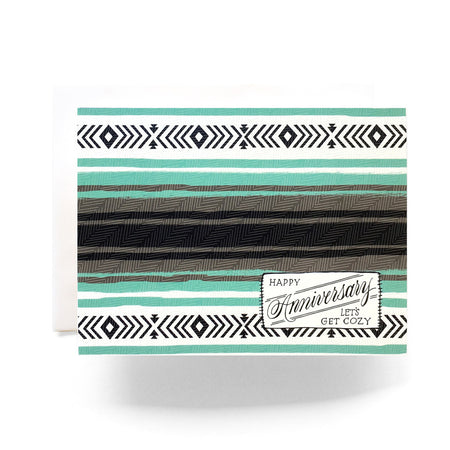 White card with images of a camp blanket in the colors of black, white, gray and teal. Black text saying, “Happy Anniversary Let’s Get Cozy”. A white envelope is included.