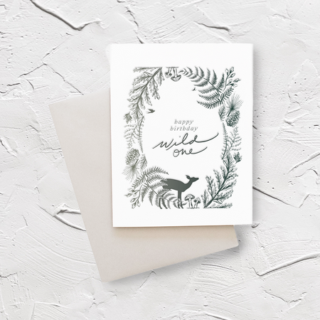 White card with green text saying, “Happy Birthday Wild One”. Images in green of a deer, mushrooms, forest greenery and pinecones. A gray envelope is included.