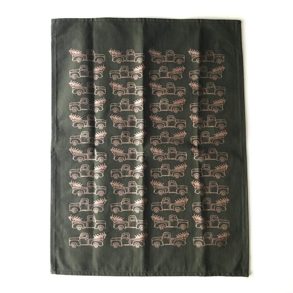 Black tea towel with images of tan holiday pickup truck with tree in the truck bed tiled across the towel.