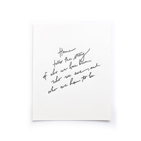 Art print with white background and black script text saying, “Home tells the story of who we have been, who we are, and who we hope to be”. 
