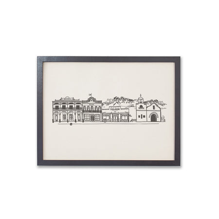 Art print with ivory background and black ink. Image of a vintage Western town with a saloon; church; bank and motel with mountains in the background.