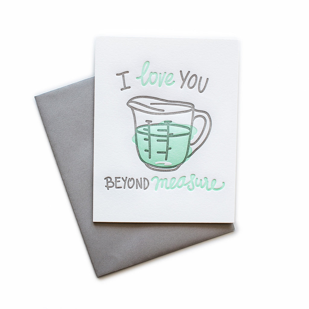 White card with gray and teal text saying, “I Love You Beyond Measure”. Image of a liquid measuring cup filled with teal liquid. A gray envelope is included.