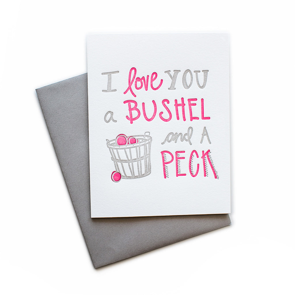 White card with gray and red text saying, “I Love You a Bushel and A Peck”. Image of a bushel basket of red apples. A gray envelope is included.