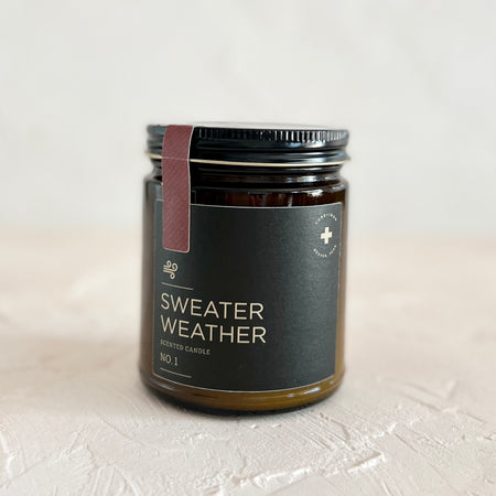 Brown jar with black lid and dark green label with white text saying, “Sweater Weather”. Images of a gust of wind.