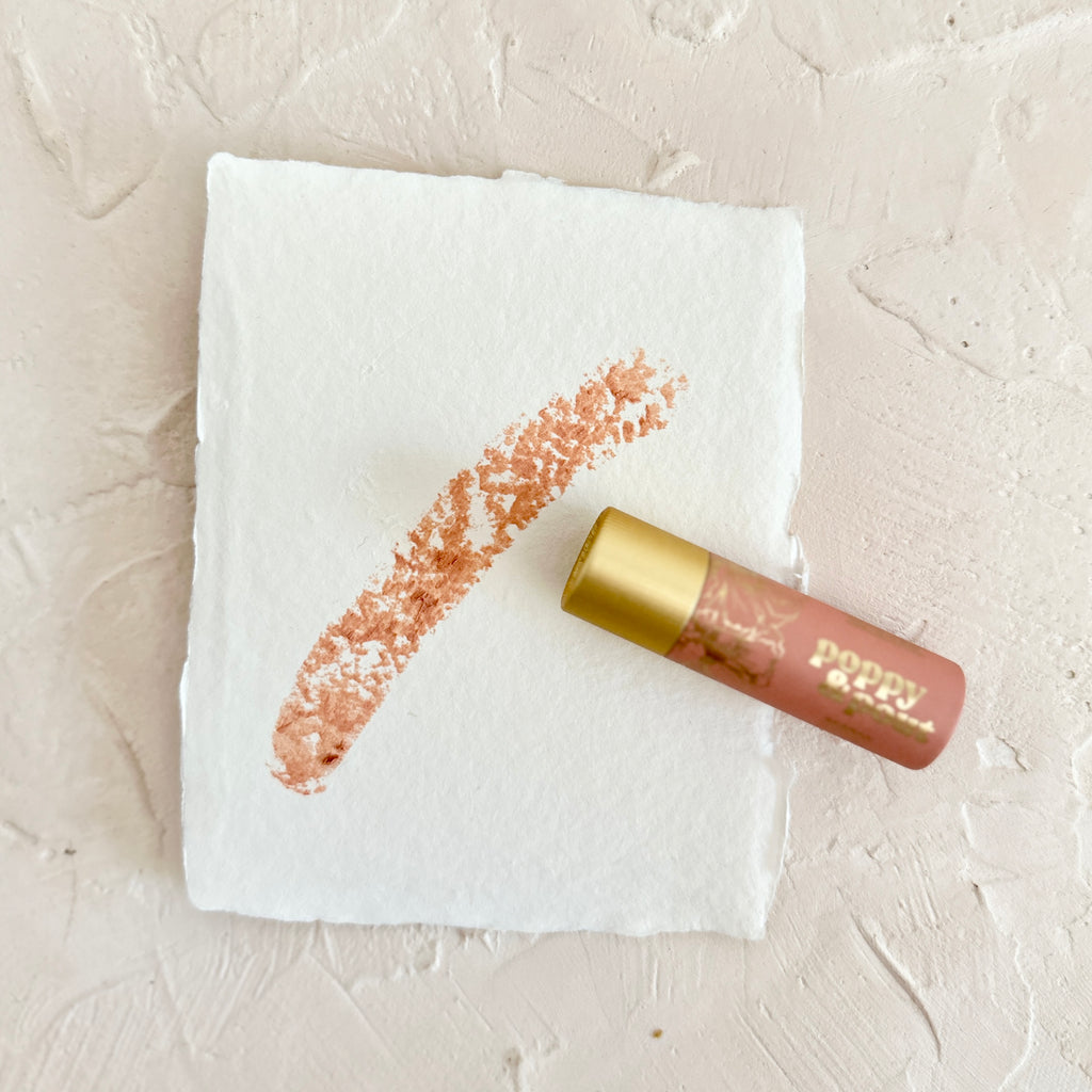 Rose colored tube with gold top and gold foil text saying, 