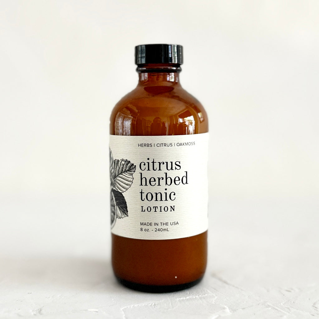 Brown bottle with black lid and white label with black text saying, “Citrus Herbed Tonic Lotion”. Image of herb leaves.