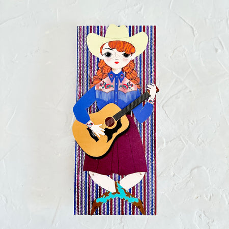 Card with red, white and blue vertical striped background with image of a cowgirl playing a guitar. 