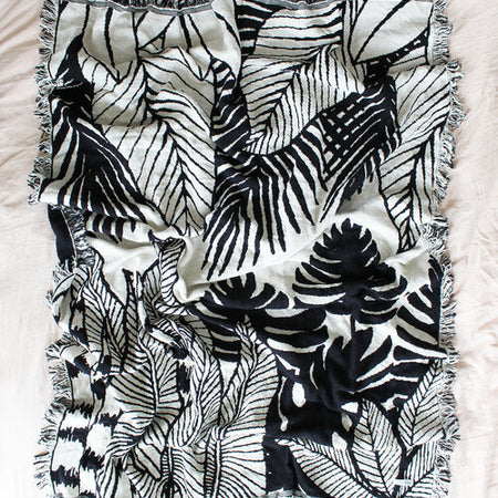 Rectangle blanket with white and black image of jungle tree leaves.
