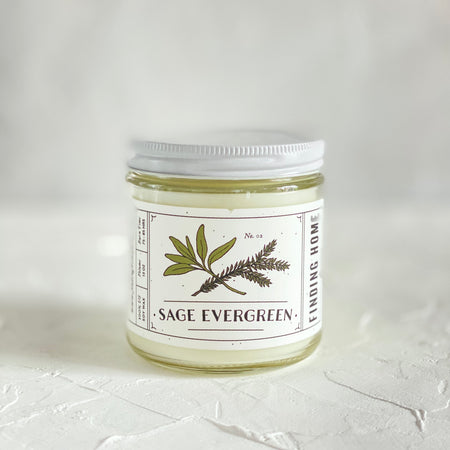 Packaged in a round glass jar with white lid. White label with black text saying, “Sage Evergreen”. Images of a sage sprig and an evergreen branch.
