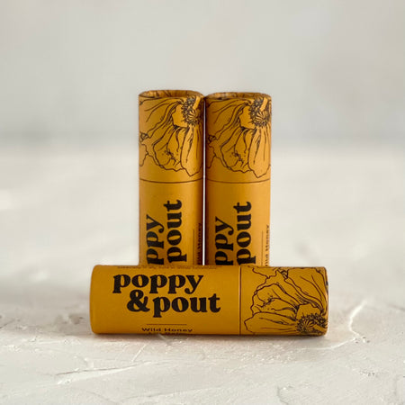 Small yellow gold tube with black text saying, “Poppy & Pout Wild Honey”. Images of black poppy flowers on top of tube.