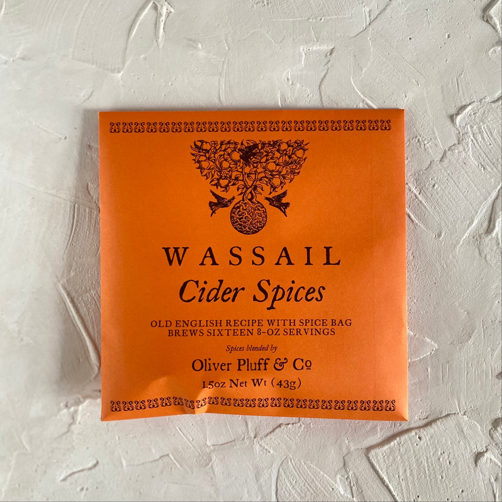 Orange packaging with black text saying, "Wassail Cider Spices". Images of two black birds flying around a black tree.