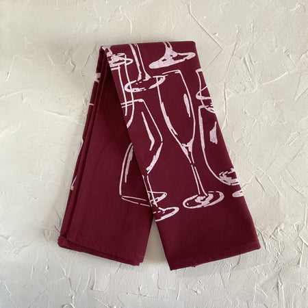 Burgundy tea towel with images of various sized wine glasses outlined in white.