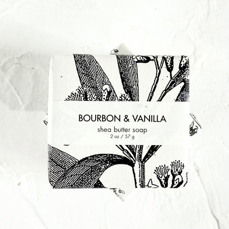White square package with black text saying, “Bourbon & Vanilla Shea Butter Soap”. Image of vanilla bean plants.