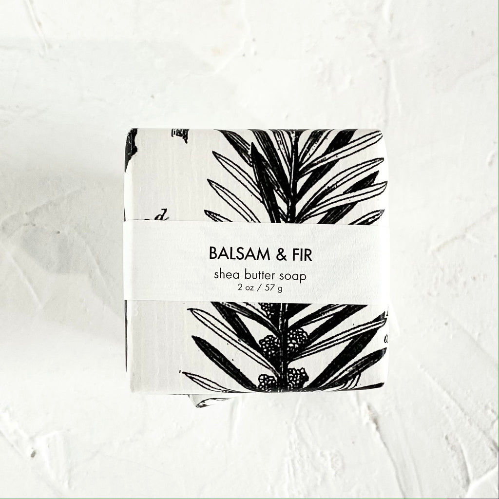 White square package with black text saying, “Balsam & Fir Shea Butter Soap”. Image of balsam and fir tree branches.