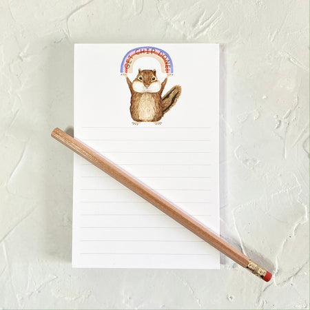 White notepad with image of a brown squirrel holding a rainbow over its head. Black text in rainbow saying, 