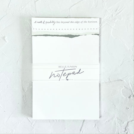 White notepad with gray text saying, “A world of possibility lies beyond the edge of the horizon” across the top.