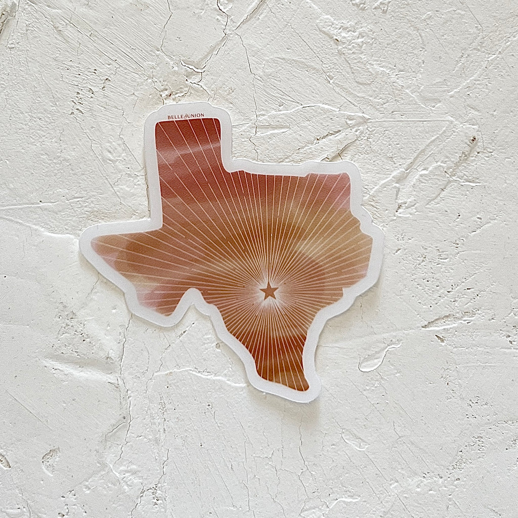 White sticker in the shape of Texas with red, white, orange and yellow rays coming out of an orange star in center of sticker.