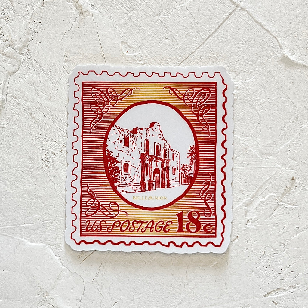 White sticker in the image of a postage stamp with red and yellow background with the Alamo in the center. Red text saying, “US Postage 18 cents”. 