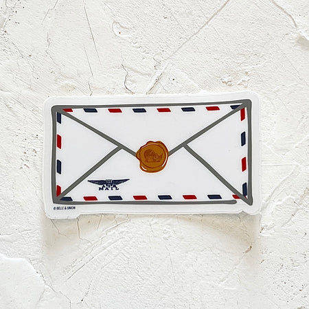 White sticker in the image of an envelope with red and blue dashes around the edge with gold seal in the middle and blue air mail stamp in left corner.