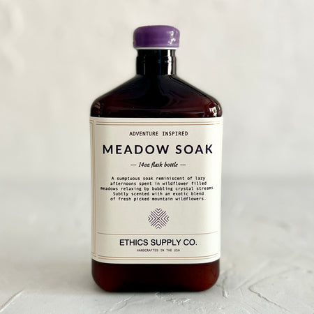 Brown square bottle with purple cap. White label with purple text saying, “Meadow Soak”. 