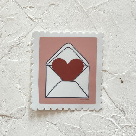White sticker in the image of a postage stamp with pink background with white mailing envelope with a red heart coming out of back flap.