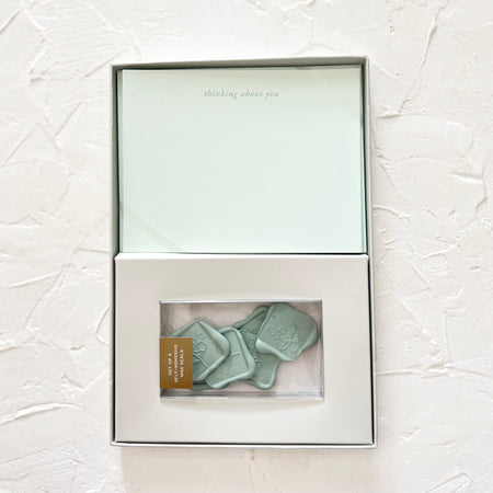 Box set of white cards with gray text saying, “Thinking About You” centered on top of card. Includes green colored wax seals.