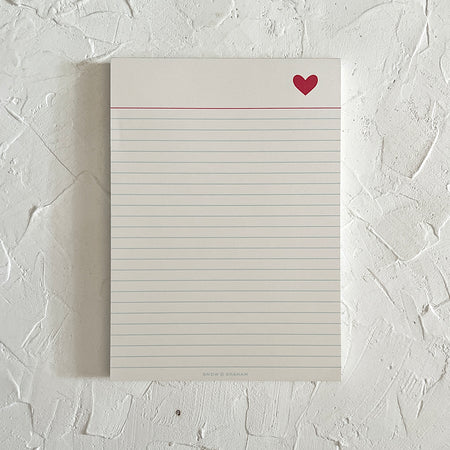White lined notebook paper notepad with white binding across the top. An image of small red heart in top corner.