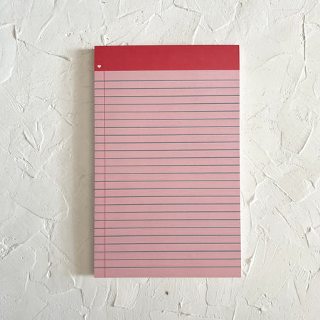 Red lined notebook paper notepad with red binding across the top. Image of small white heart in upper left corner.