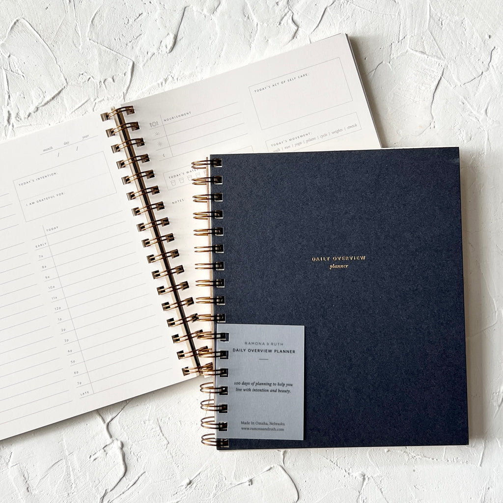Black cover with gold foil text saying, "Daily Overview Planner". Gold coil binding on left side.