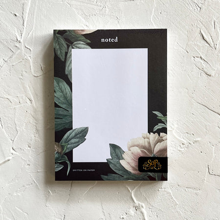Notepad with black border and floral design with white rectangle in the middle.