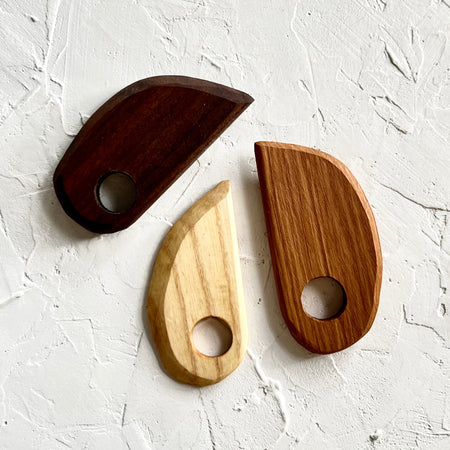 Wooden dough scraper with carved edges and hole for holding.