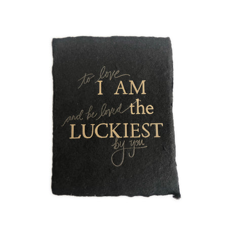 Black textured card with gold text saying, “I Am the Luckiest to Love and Be Loved By You”. A gray envelope is included.
