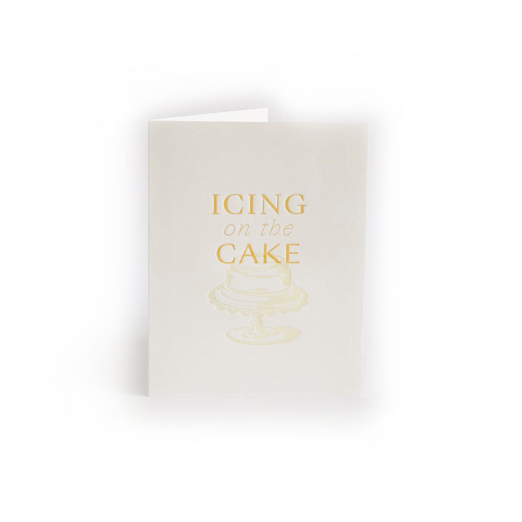 Ivory card with gold text saying, “Icing on the Cake”. Image of a two tier wedding cake on a pedestal dish. A gray envelope is included.