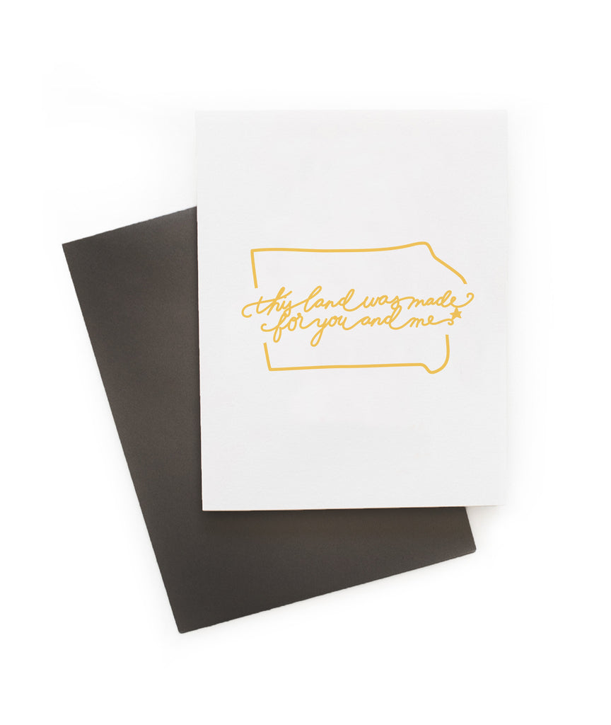 White card with yellow text saying, “This Land is Made for You and Me”. Yellow outline image of the state of Kansas. A gray envelope is included.