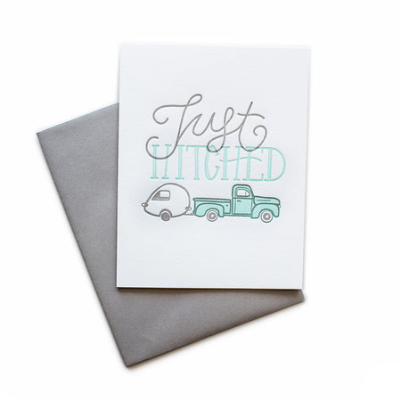 White card with gray and teal text saying, “Just Hitched”. Images of a teal pickup truck towing a vintage camper. A gray envelope is included.