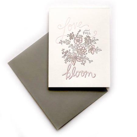 White card with gray and pink text saying, “Love is in Full Bloom”. Images of pink and gray flowers. A gray envelope is included.